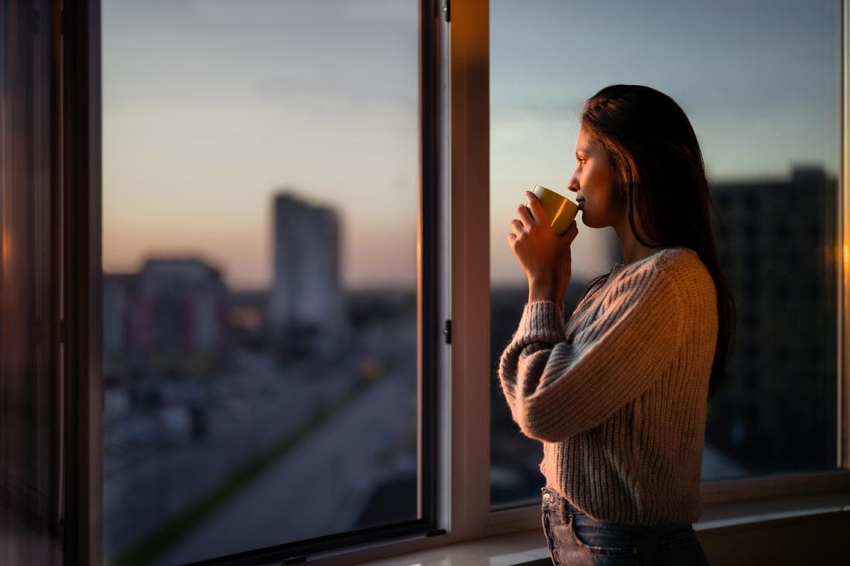 Person beginning a quiet morning beside a sunlit window, reflecting on who they are becoming